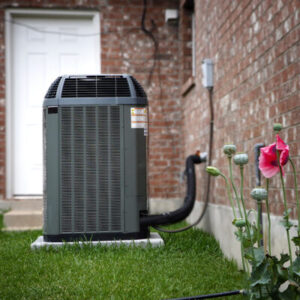A residential HVAC unit situated in the grass outside a brick home