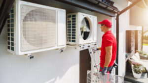 A worker in a red shirt looks at an HVAC unit